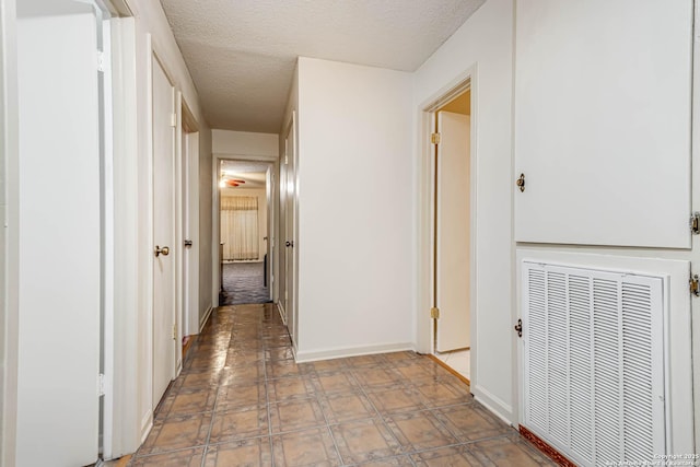 hallway featuring baseboards, a textured ceiling, and tile patterned floors