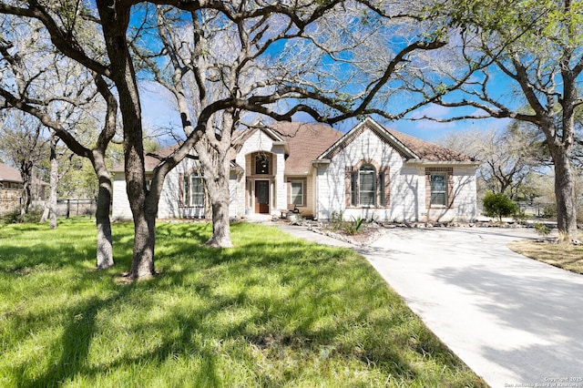 french provincial home with driveway, brick siding, fence, and a front yard