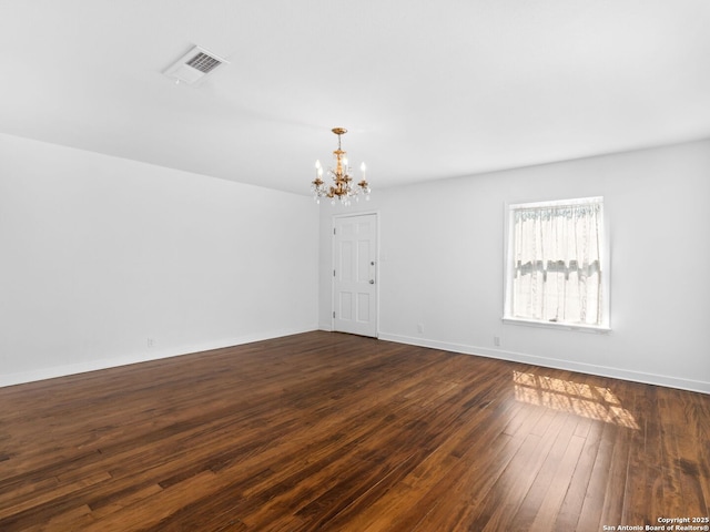 spare room featuring dark wood-type flooring, visible vents, baseboards, and an inviting chandelier