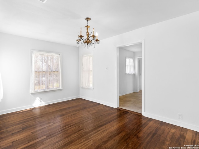 unfurnished room featuring a notable chandelier, baseboards, and wood finished floors