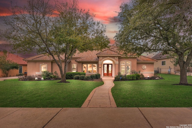 mediterranean / spanish house featuring french doors, a yard, stucco siding, fence, and a tiled roof