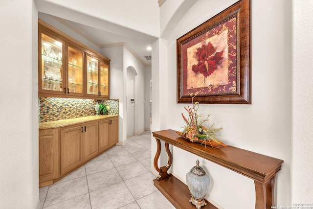 bar with light tile patterned floors, baseboards, arched walkways, ornamental molding, and backsplash