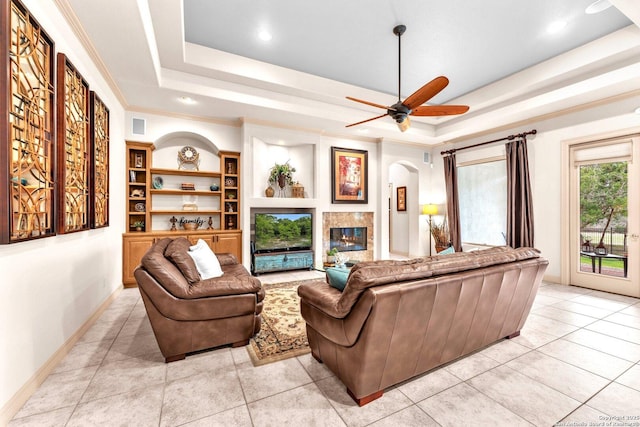 living room featuring light tile patterned floors, a raised ceiling, a premium fireplace, ornamental molding, and baseboards