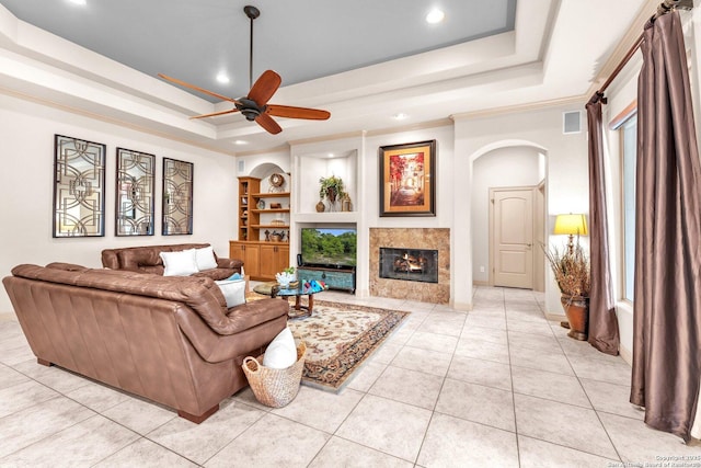 living room featuring arched walkways, a tray ceiling, a fireplace, and light tile patterned floors