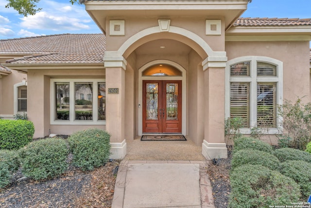 view of exterior entry featuring a tile roof, french doors, and stucco siding