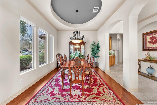 dining room with light wood-type flooring, a raised ceiling, visible vents, and arched walkways