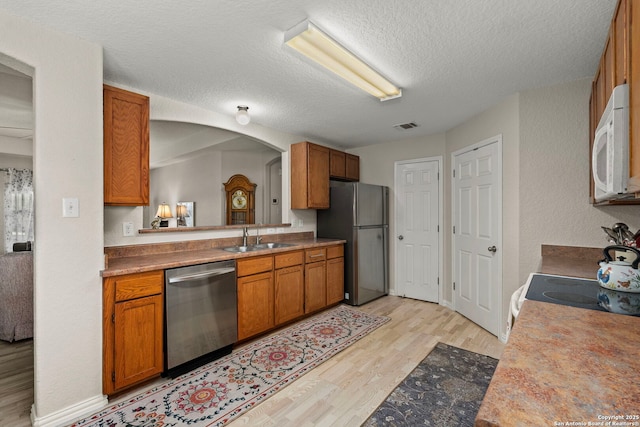 kitchen featuring brown cabinets, light wood finished floors, stainless steel appliances, and a sink