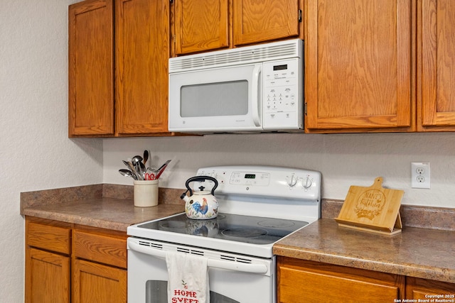 kitchen with white appliances, brown cabinetry, and dark countertops