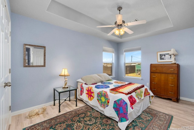 bedroom featuring baseboards, a tray ceiling, ceiling fan, and wood finished floors