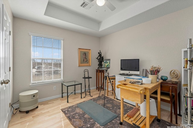 office with a tray ceiling, wood finished floors, visible vents, and baseboards