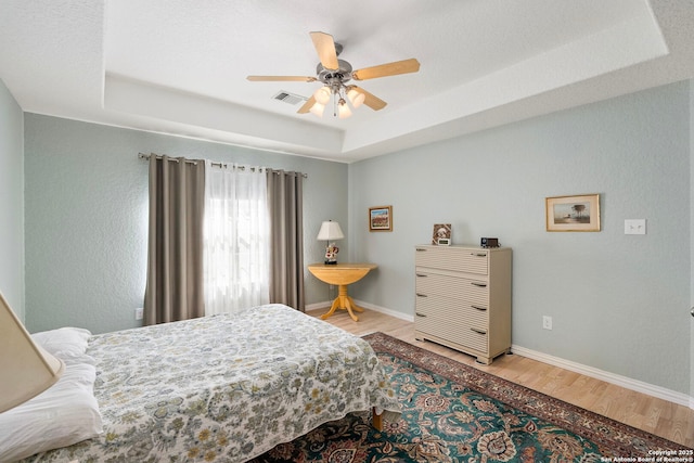 bedroom featuring wood finished floors, a raised ceiling, visible vents, and baseboards