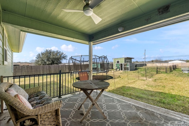 view of patio with a trampoline, an outbuilding, a fenced backyard, and ceiling fan