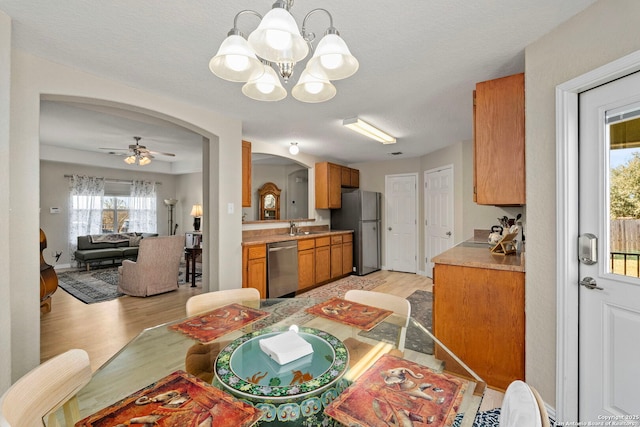 dining room with light wood-style floors, arched walkways, a textured ceiling, and ceiling fan with notable chandelier