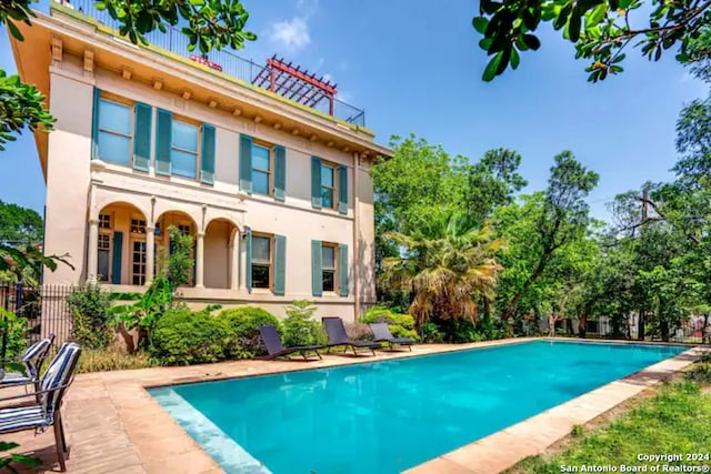 back of house featuring fence, an outdoor pool, and stucco siding