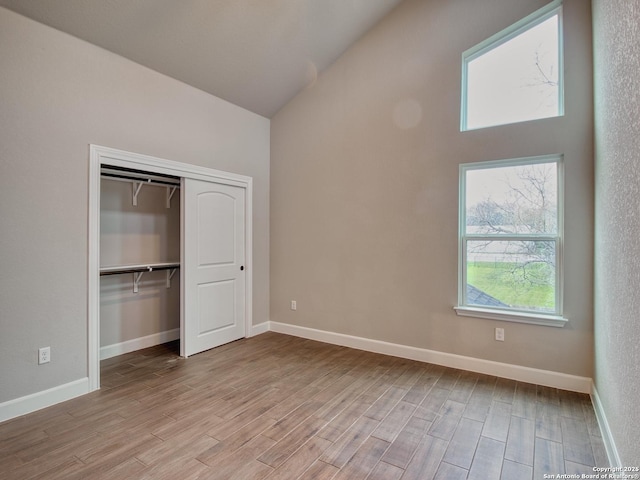 unfurnished bedroom with high vaulted ceiling, a closet, wood finished floors, and baseboards