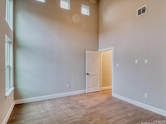 spare room featuring light wood-type flooring, a towering ceiling, visible vents, and baseboards