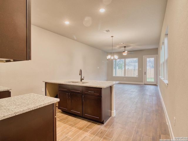 kitchen with dark brown cabinetry, wood finish floors, a sink, visible vents, and an inviting chandelier