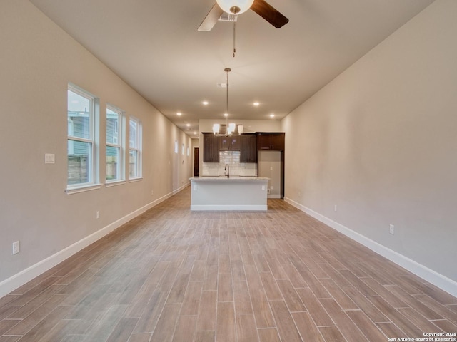 unfurnished living room with light wood-style flooring, baseboards, a sink, and ceiling fan with notable chandelier