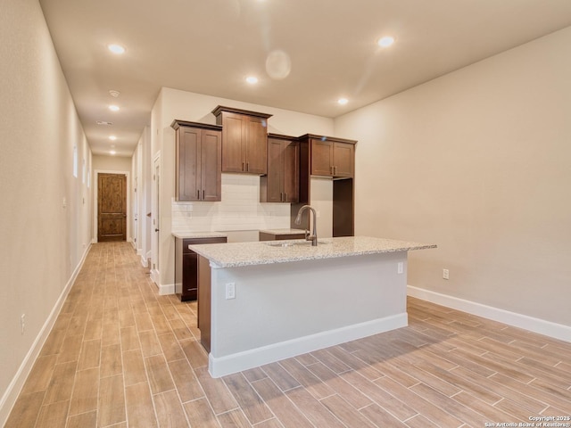 kitchen featuring a kitchen island with sink, recessed lighting, wood finish floors, a sink, and tasteful backsplash