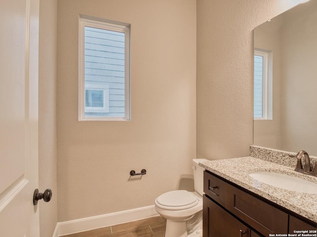 half bathroom with toilet, wood finished floors, vanity, a healthy amount of sunlight, and baseboards