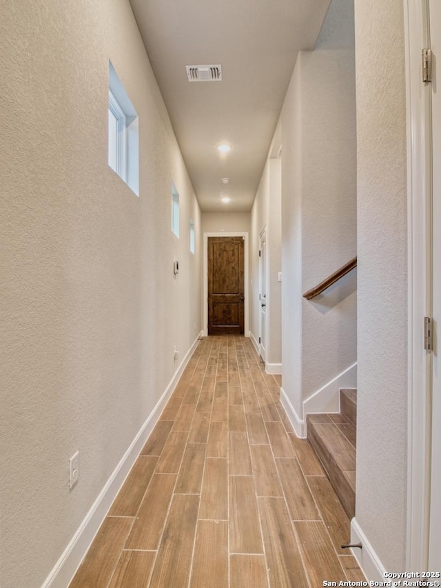 hall featuring wood finish floors, visible vents, baseboards, and stairs