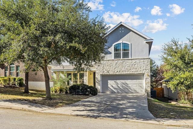 traditional-style house with a garage, central AC unit, concrete driveway, stone siding, and stucco siding