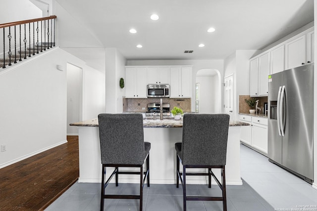 kitchen featuring visible vents, arched walkways, a kitchen island with sink, stainless steel appliances, and stone counters