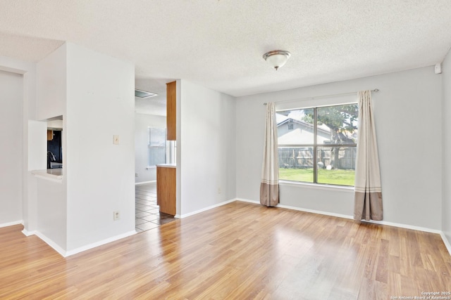 empty room featuring a textured ceiling, baseboards, and wood finished floors