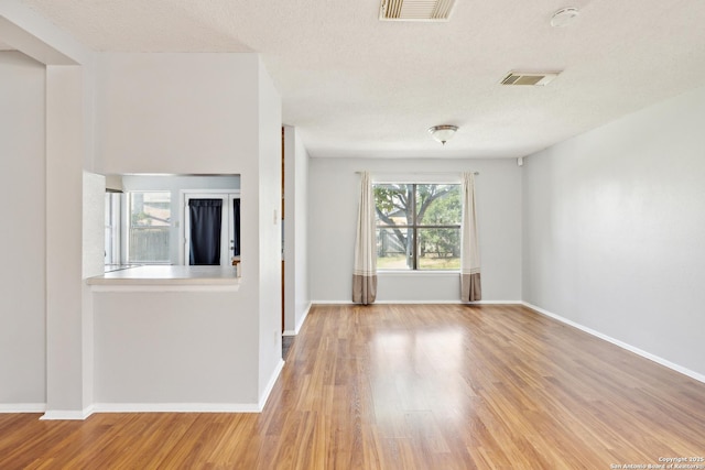 unfurnished room with a textured ceiling, wood finished floors, and visible vents