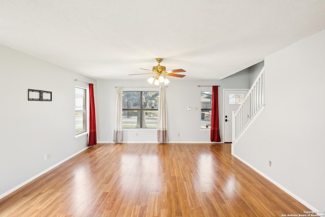 unfurnished living room featuring light wood-type flooring, ceiling fan, baseboards, and stairs