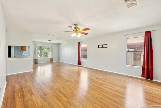 empty room with light wood finished floors, visible vents, a ceiling fan, a textured ceiling, and baseboards