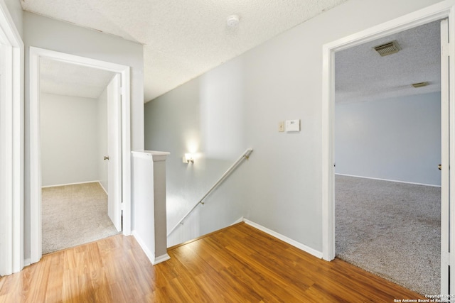 hall featuring carpet floors, a textured ceiling, an upstairs landing, and wood finished floors