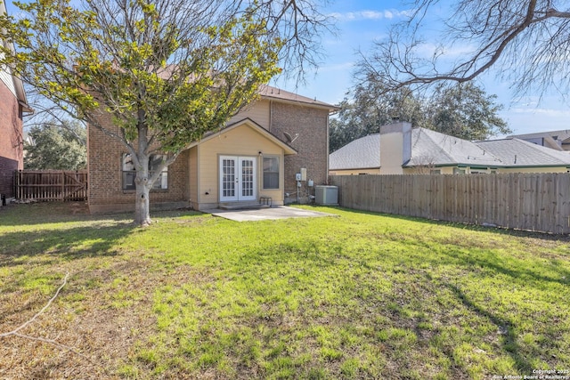 rear view of property with cooling unit, a fenced backyard, brick siding, french doors, and a lawn