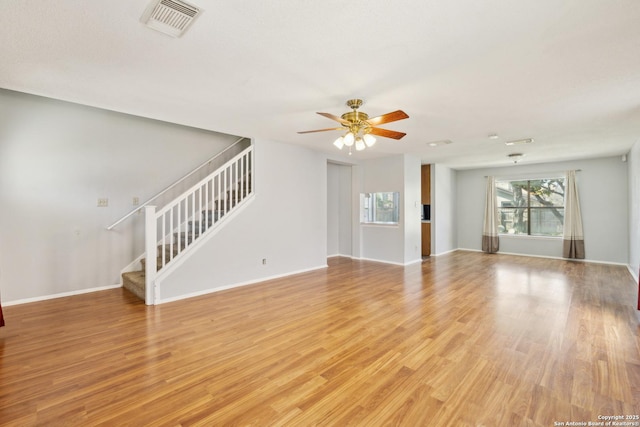 unfurnished living room with ceiling fan, light wood-style flooring, visible vents, baseboards, and stairway