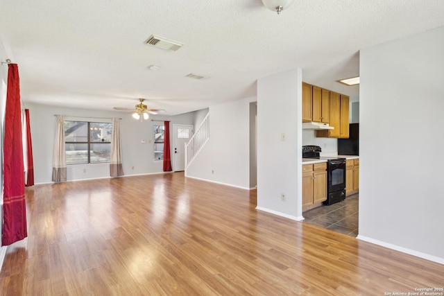 unfurnished living room featuring light wood finished floors, visible vents, ceiling fan, stairway, and a textured ceiling