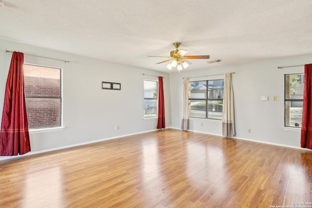 empty room with visible vents, baseboards, a ceiling fan, light wood-style flooring, and a textured ceiling