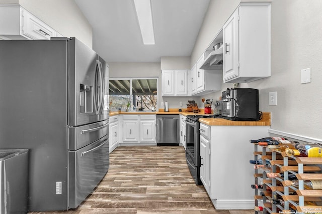 kitchen featuring stainless steel appliances, white cabinetry, a sink, wood finished floors, and exhaust hood