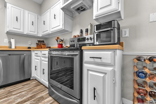 kitchen with appliances with stainless steel finishes, white cabinetry, light wood finished floors, and custom exhaust hood