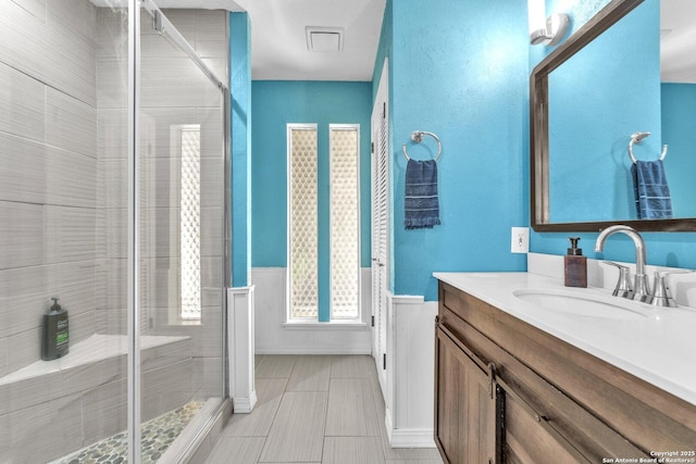 bathroom featuring a stall shower, wainscoting, and vanity