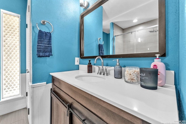 bathroom with a textured wall, a shower with door, and vanity