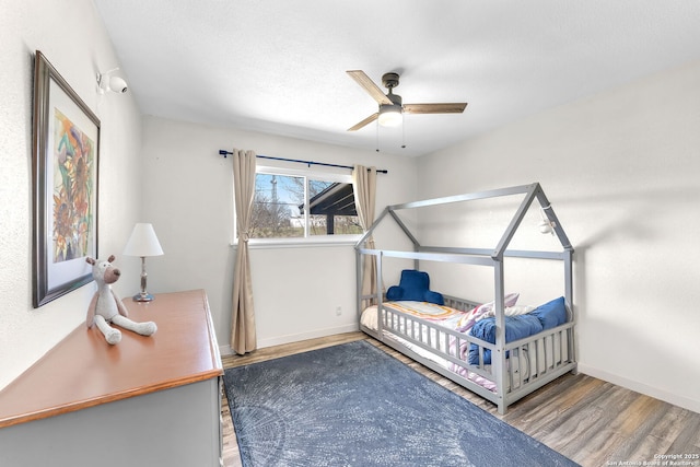 bedroom with a ceiling fan, a textured ceiling, baseboards, and wood finished floors