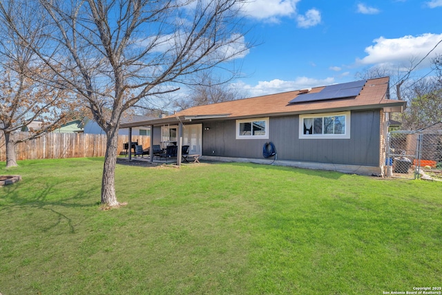 rear view of property featuring a yard, a patio, a fenced backyard, and roof mounted solar panels