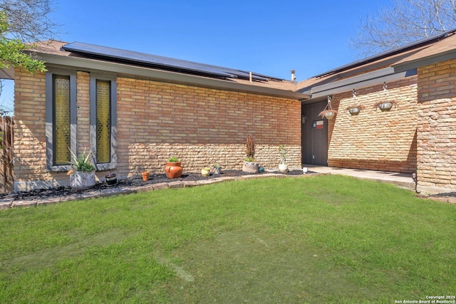 entrance to property with solar panels, brick siding, and a lawn