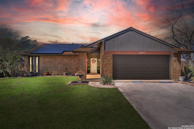 mid-century inspired home featuring a garage, brick siding, driveway, a lawn, and roof mounted solar panels