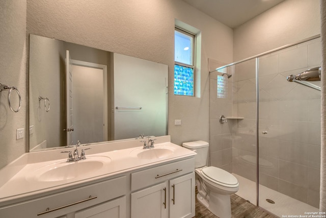 full bath featuring toilet, double vanity, a tile shower, and a sink