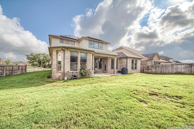 rear view of property featuring a patio, a fenced backyard, brick siding, a yard, and roof mounted solar panels