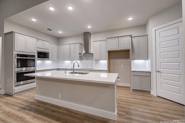 kitchen featuring a sink, light wood-style floors, light countertops, appliances with stainless steel finishes, and wall chimney exhaust hood