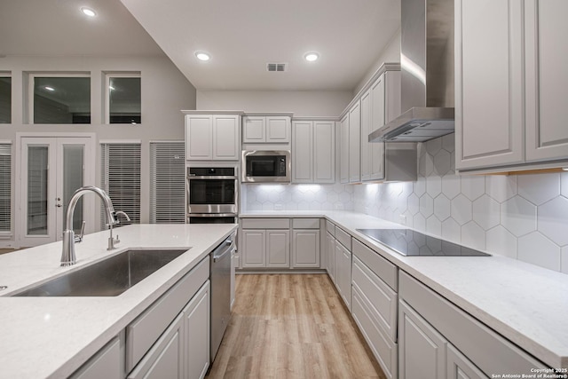 kitchen with visible vents, wall chimney exhaust hood, light wood-style flooring, appliances with stainless steel finishes, and a sink