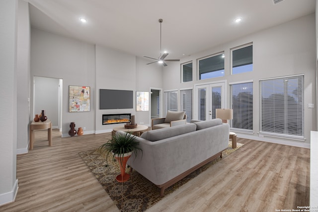 living room with baseboards, a glass covered fireplace, a towering ceiling, light wood-style flooring, and french doors