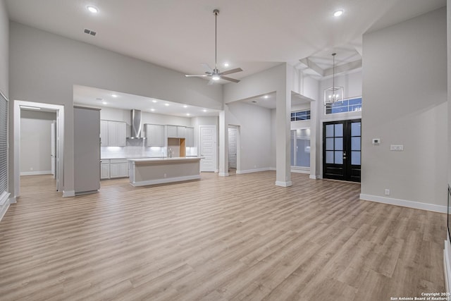 unfurnished living room with french doors, a high ceiling, light wood-style flooring, and baseboards